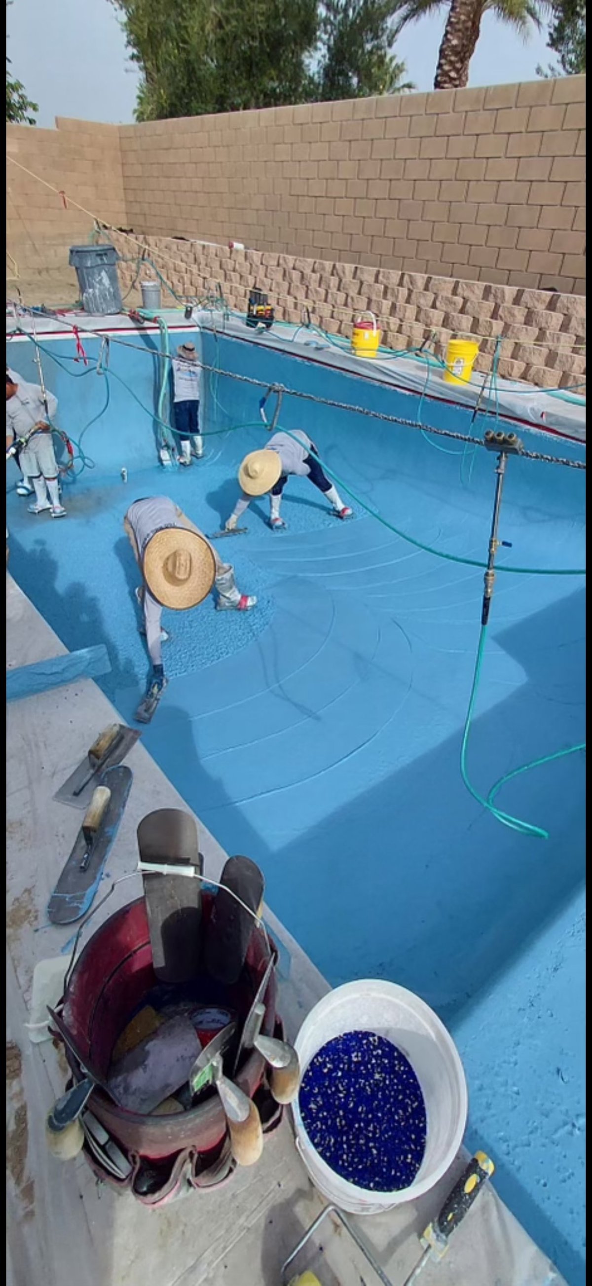 Workers painting a large blue pool or water tank with construction materials and supplies visible nearby