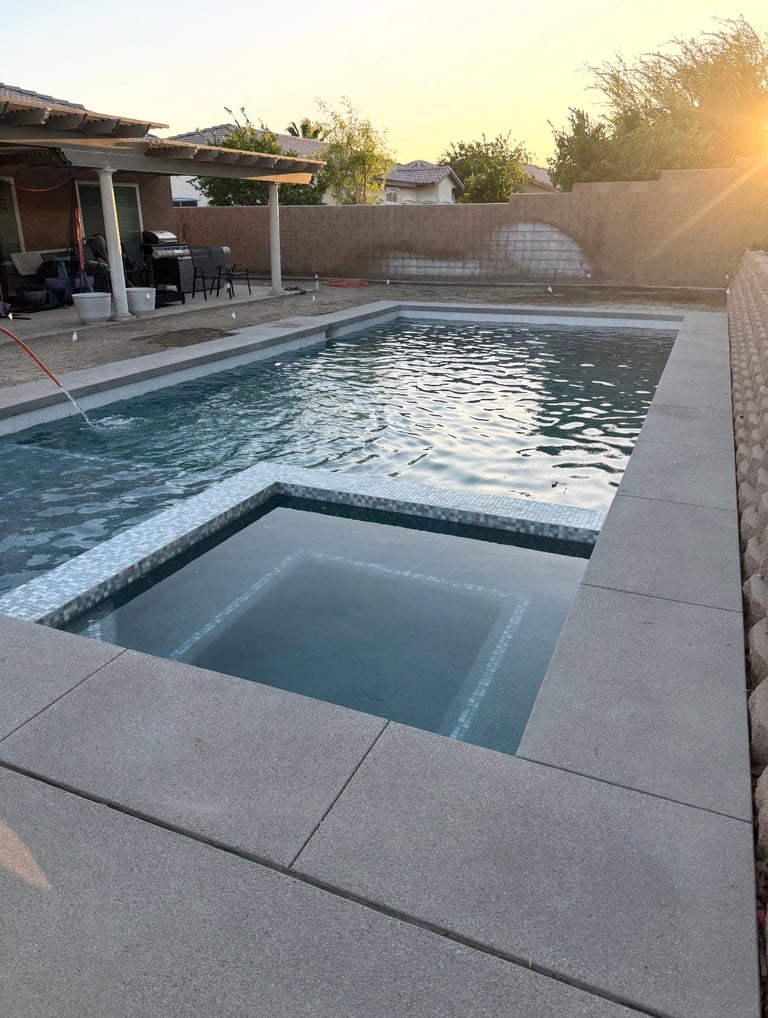 Modern backyard swimming pool with attached spa at sunset, concrete deck, and covered patio area