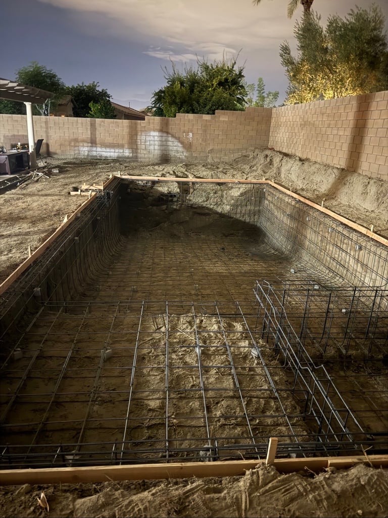 Residential pool under construction with concrete foundation, rebar grid, and brick walls in early building stage
